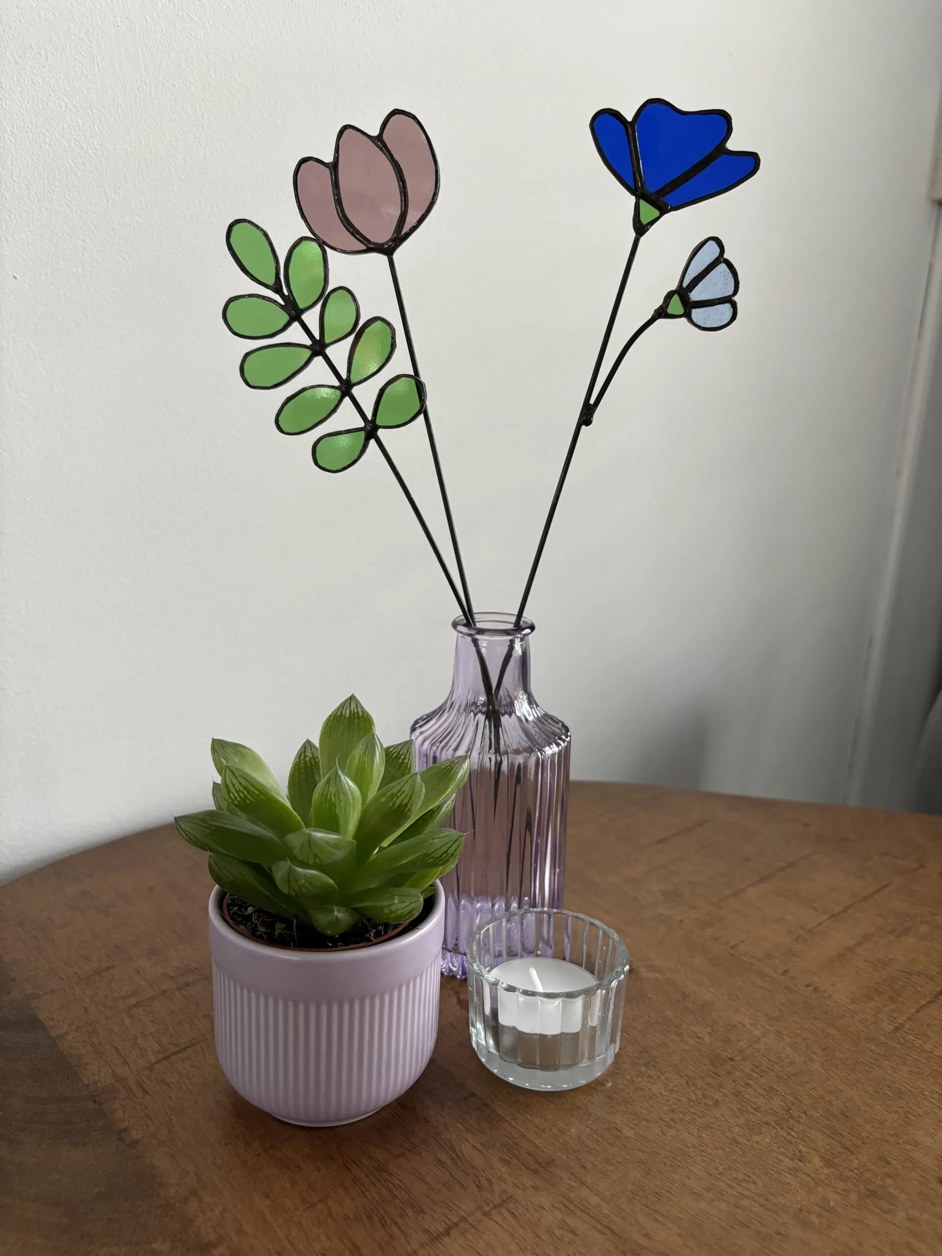 Tiffany glaskunst: paarse tulp in een vaasje met een blauwe 3-bloemblad + bloem een 9-blad tak met ronde blaadjes, beide bevestigd op een steel.