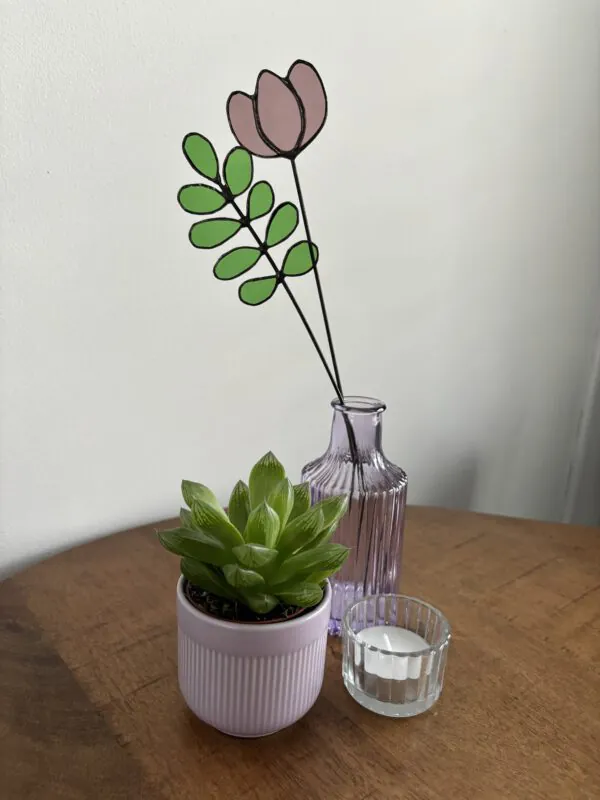 Tiffany glaskunst: paarse tulp in een vaasje met een 9-blad tak met ronde blaadjes, beide bevestigd op een steel.