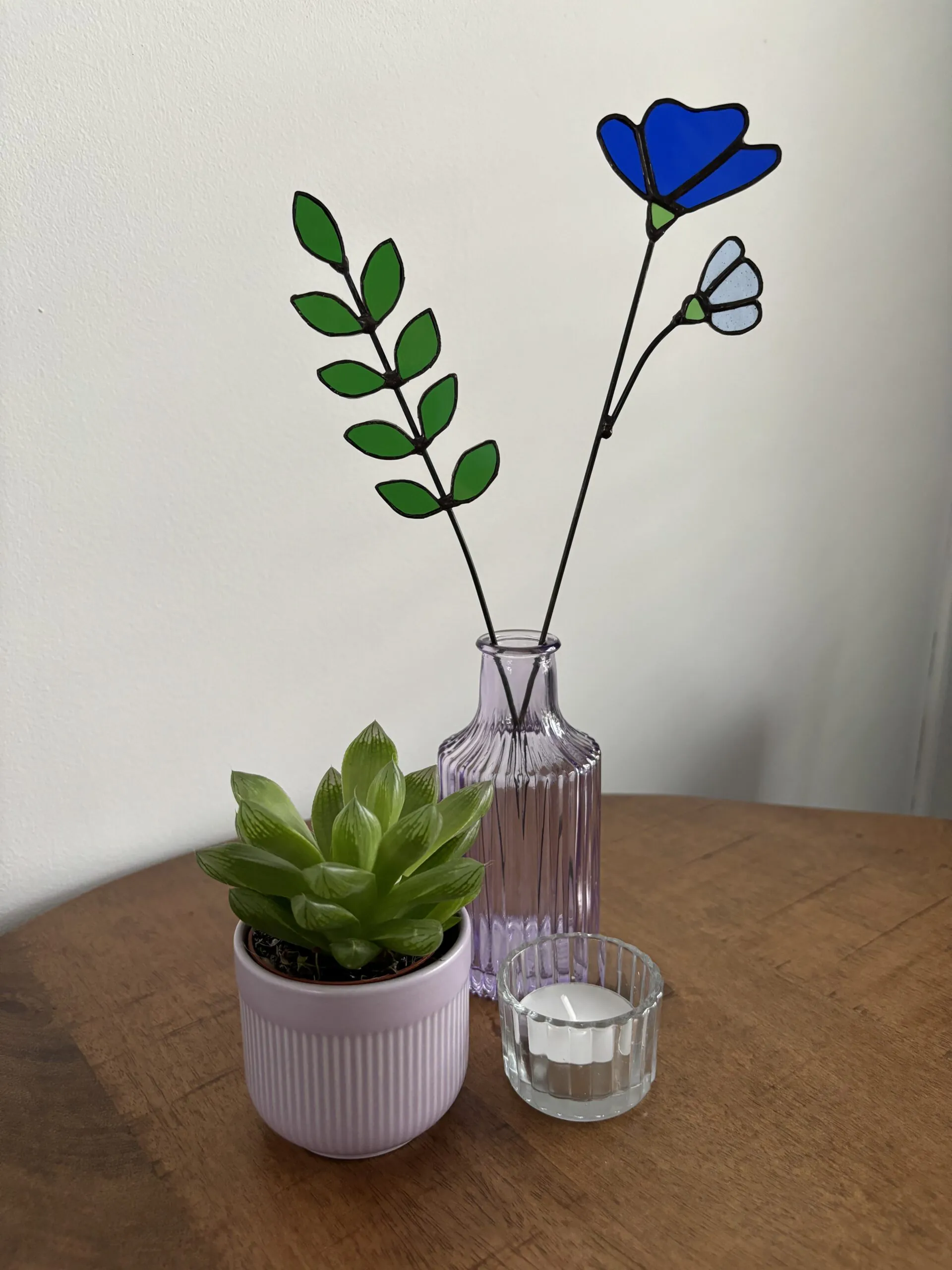 Tiffany glaskunst: 9-blad tak in een vaasje met een blauwe 3-bloemblad + bloem, beide bevestigd op een steel.