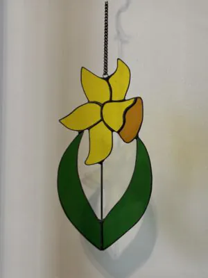 Glas in lood hanger: een gele narcis met donker groene bladeren.
