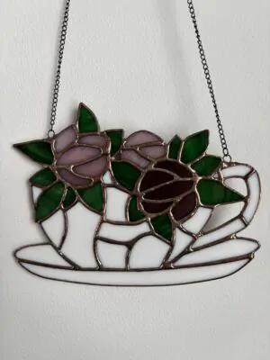 Glas in lood hanger: wit kopje met schotel en met roze en paarse bloemen.