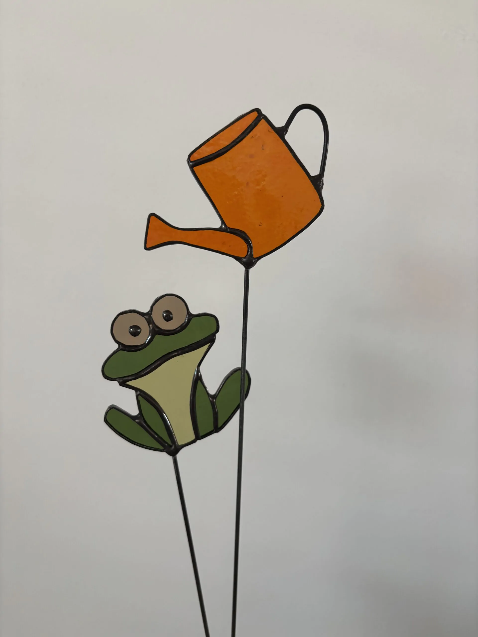 Tiffany glaskunst: een groene kikker op een steel en een oranje gieter op een steel.