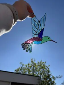 Glas in lood hanger: een kolibrie met de kleuren groen, blauw en magenta.