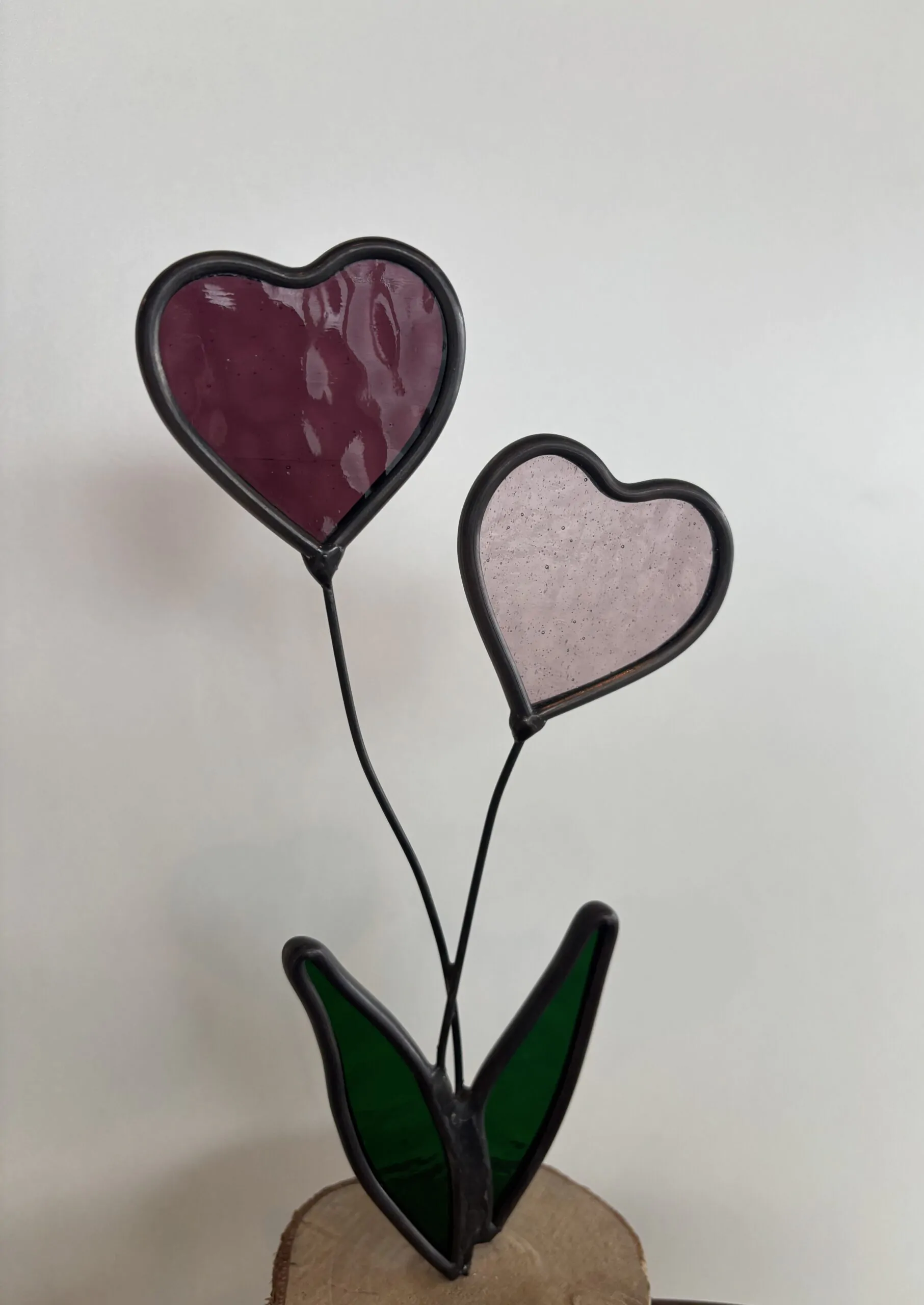 Glas in lood: 2 hartjes op steeltjes met onderaan 2 blaadjes, als geheel op een houten schijfje.