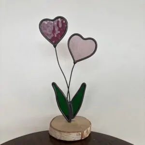 Glas in lood: 2 hartjes op steeltjes met onderaan 2 blaadjes, als geheel op een houten schijfje.