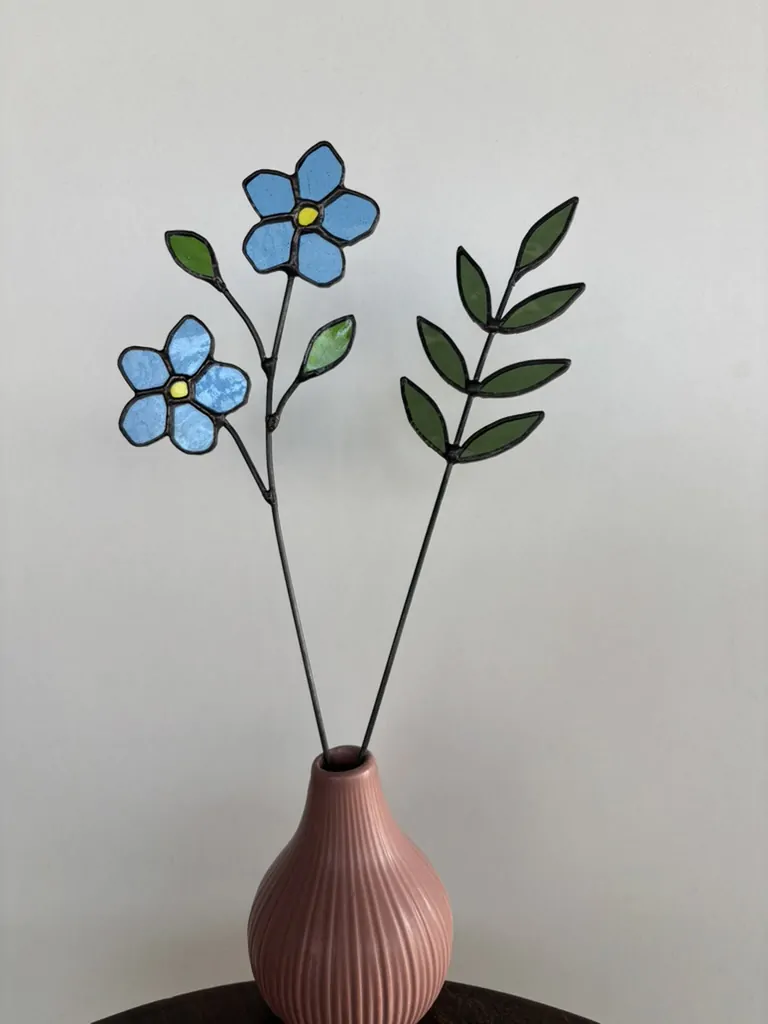 Tiffany glaskunst: sfeerfoto met een tak met 2 blauwe vergeet-mij-nietjes, 2 groene blaadjes en een olijf groene 7-blad tak.