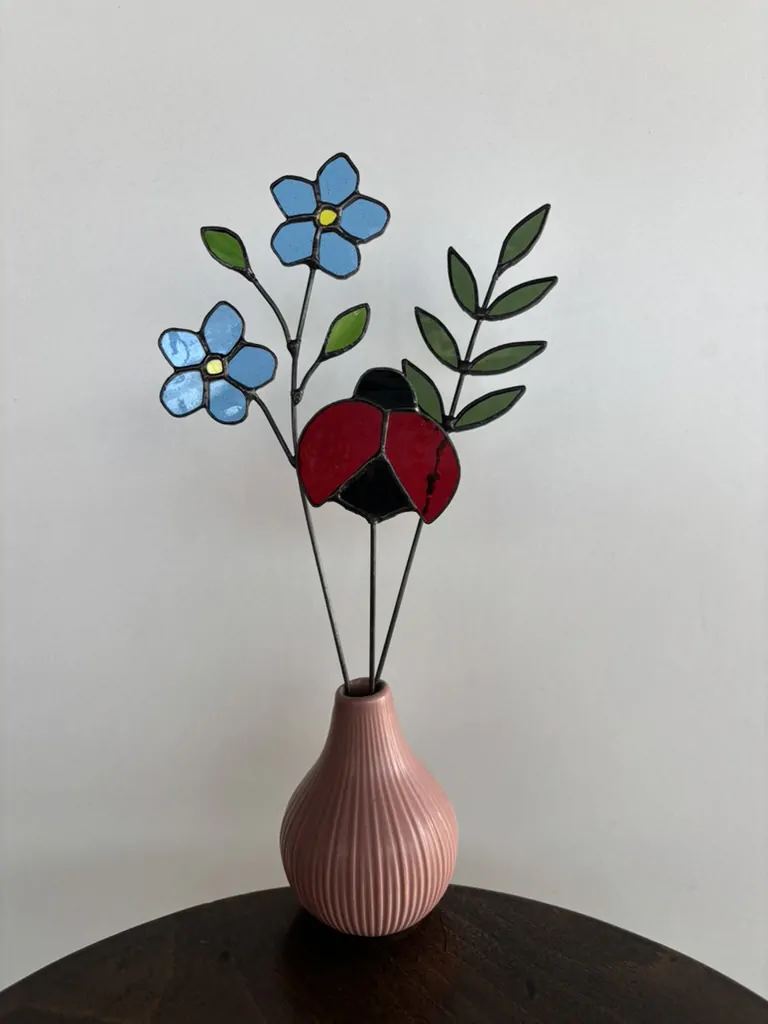 Tiffany glaskunst: sfeerfoto met een tak met 2 blauwe vergeet-mij-nietjes, 2 groene blaadjes. En een olijf groene 7-blad tak en een lieveheersbeestje op steel.